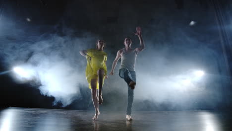 A-man-and-a-woman-dance-together-a-funny-dance-in-jeans-and-a-yellow-dress-on-stage-in-smoke.-Musical.